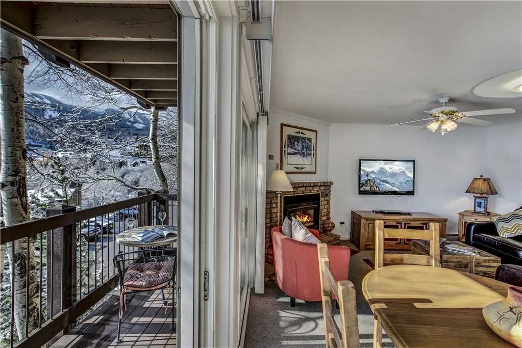 A cozy living room with a fireplace, a television, and a balcony overlooking a snowy mountain landscape.