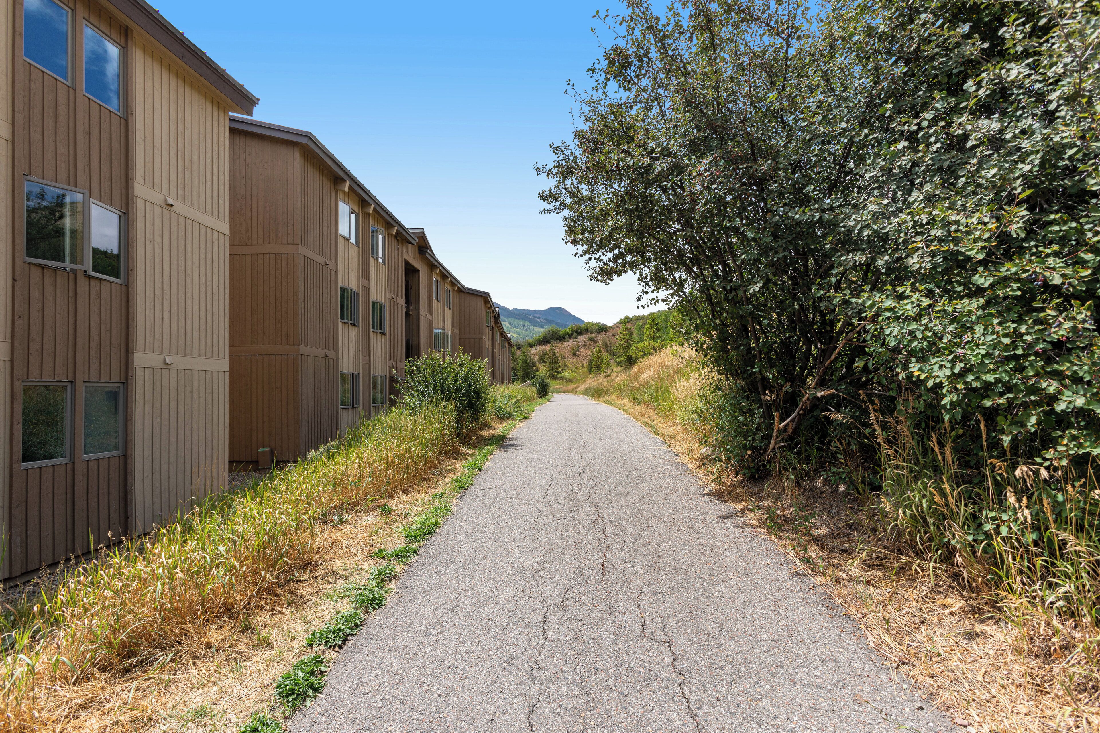 A pathway flanked by wooden buildings with multiple windows, leading towards a hilly landscape.