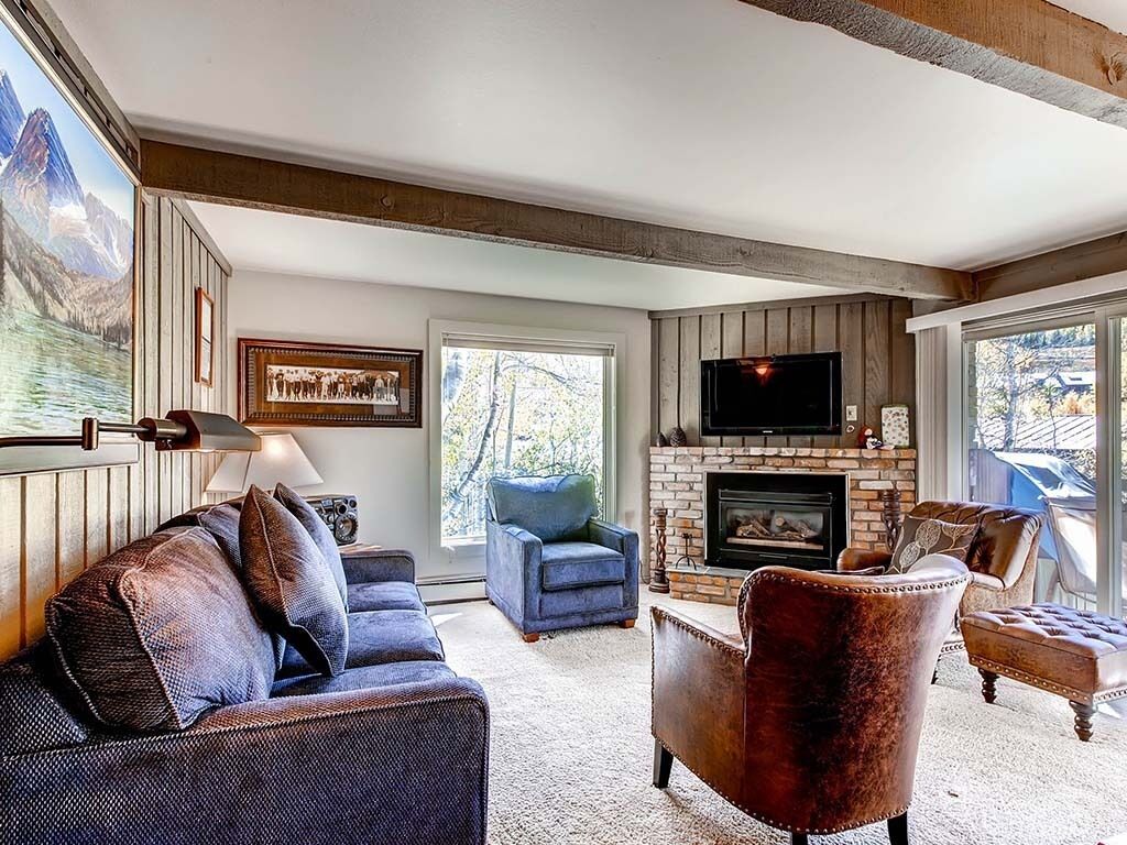 A cozy living room with a fireplace, a large window, and a mounted TV.