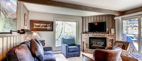 A cozy living room with a fireplace, a large window, and a mounted TV.