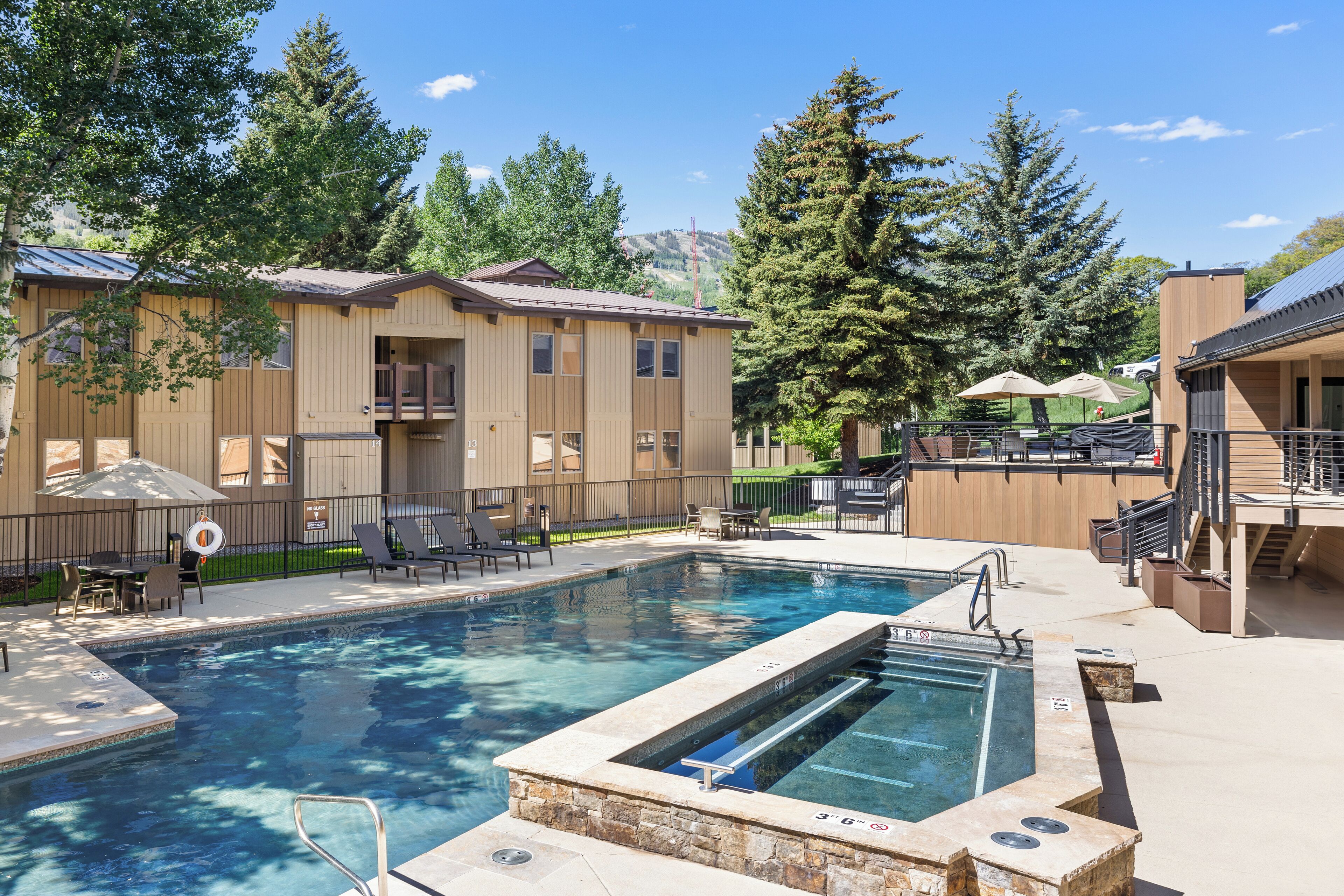 Una piscina con jacuzzi, sillas de descanso y sombrillas.