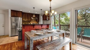 A spacious kitchen with wooden cabinets, a stainless steel refrigerator, and a large dining table set for six. - Woodbridge Condos by Snowmass Vacations (Snowmass Village)