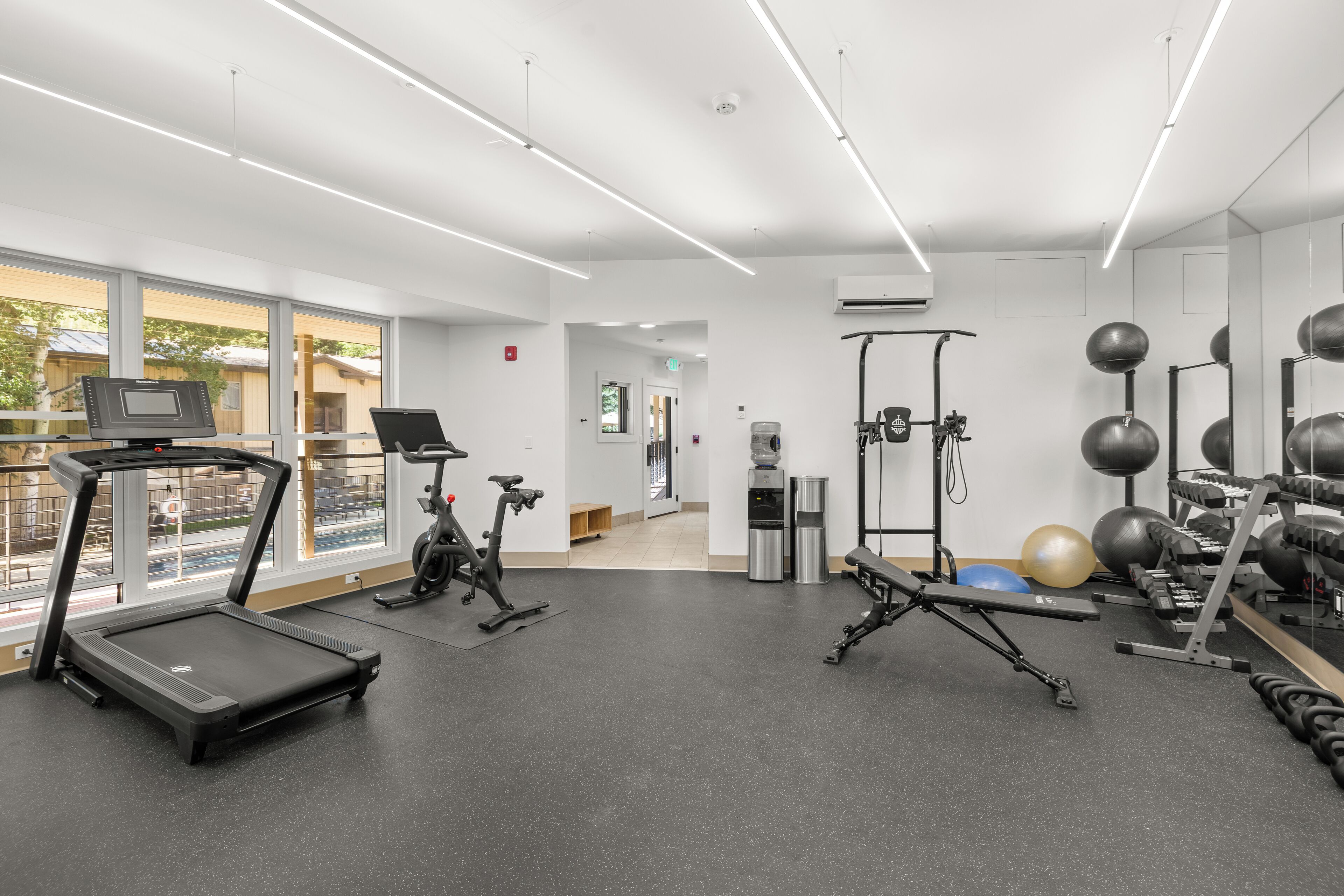 A modern gym with treadmills, elliptical machines, free weights, and exercise balls.