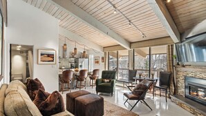 A spacious living room with a fireplace, comfortable seating, and a kitchen area visible through an open door. - Woodbridge Condos by Snowmass Vacations (Snowmass Village)