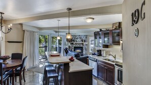 A spacious kitchen with a central island, a dining area with a round table, and a stone fireplace. - Woodbridge Condos by Snowmass Vacations (Snowmass Village)
