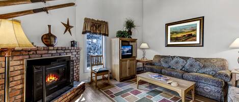 A cozy living room with a fireplace, a patterned rug, a sofa, and a television.