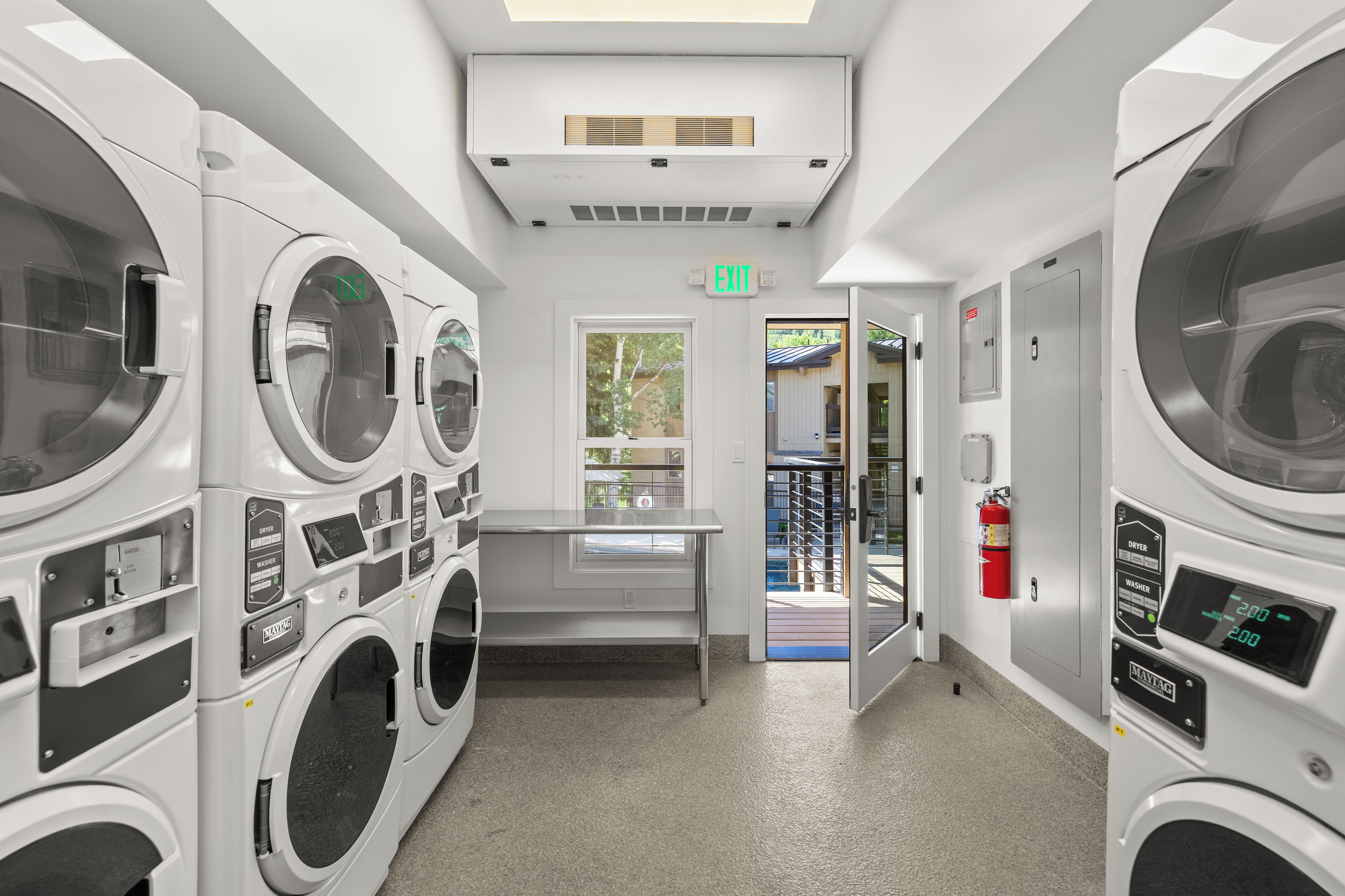 A laundry facility with multiple washing machines, a table, and an exit door.