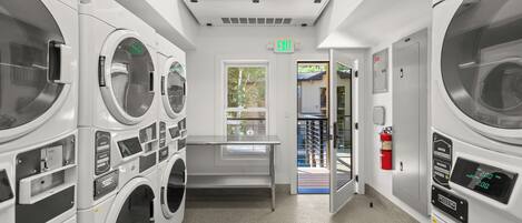 A laundry facility with multiple washing machines, a table, and an exit door.