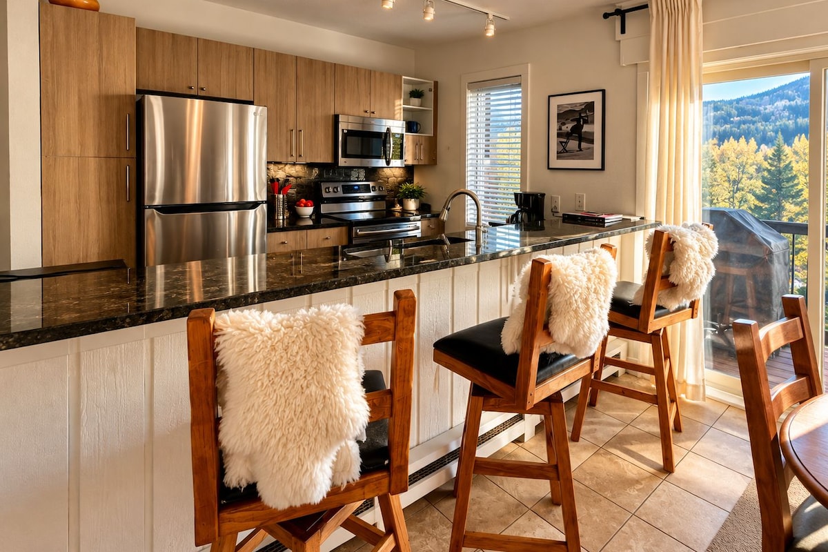 A modern kitchen with stainless steel appliances, wooden cabinets, and a bar area with high stools.