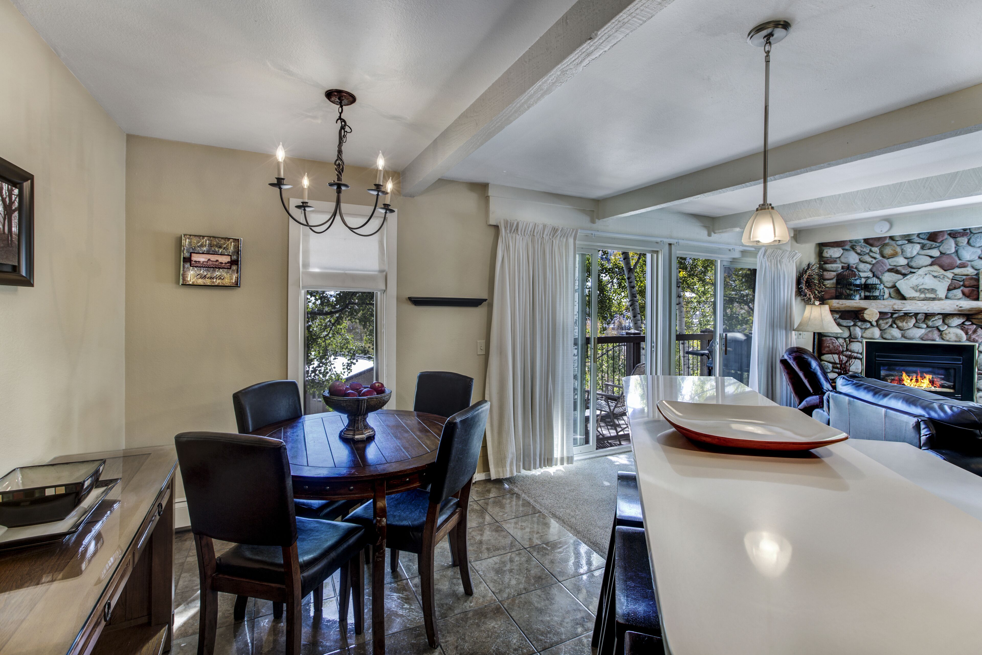 Un comedor con una mesa de madera, sillas, una araña y una chimenea.