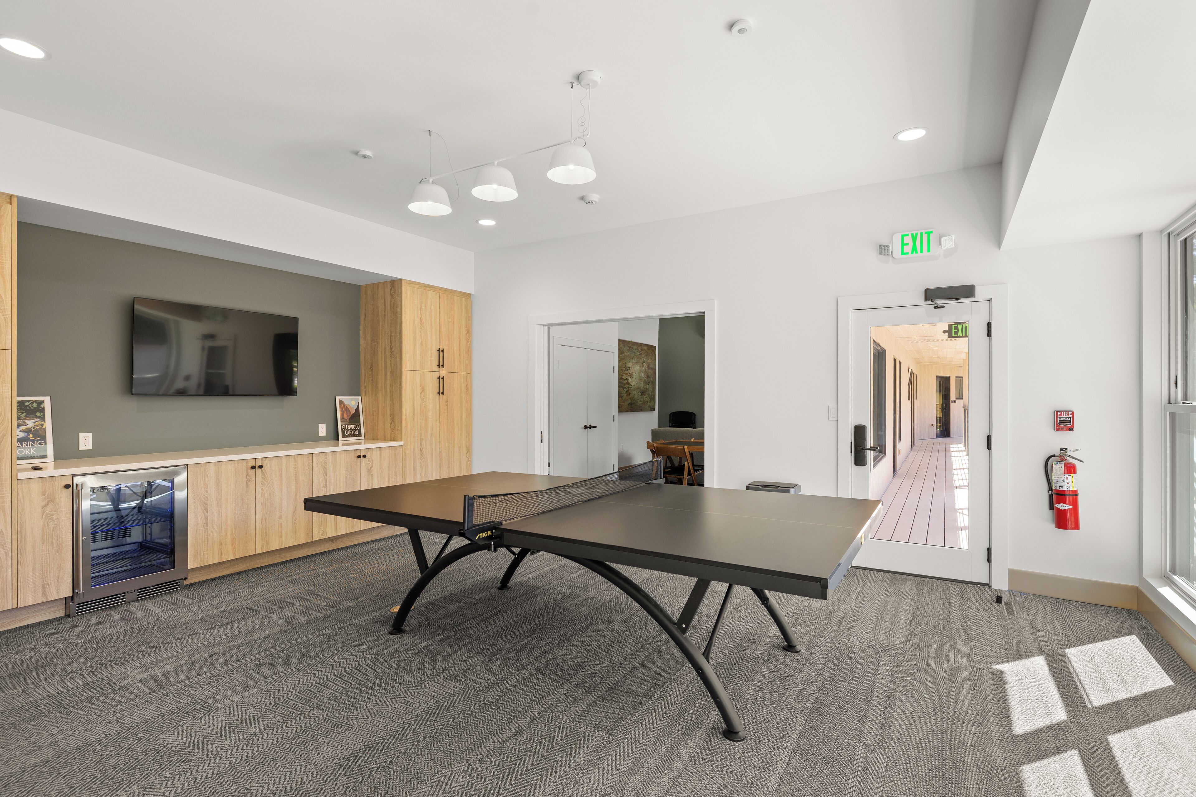 A modern conference room with a large table, wooden cabinets, a refrigerator, and a fire extinguisher.