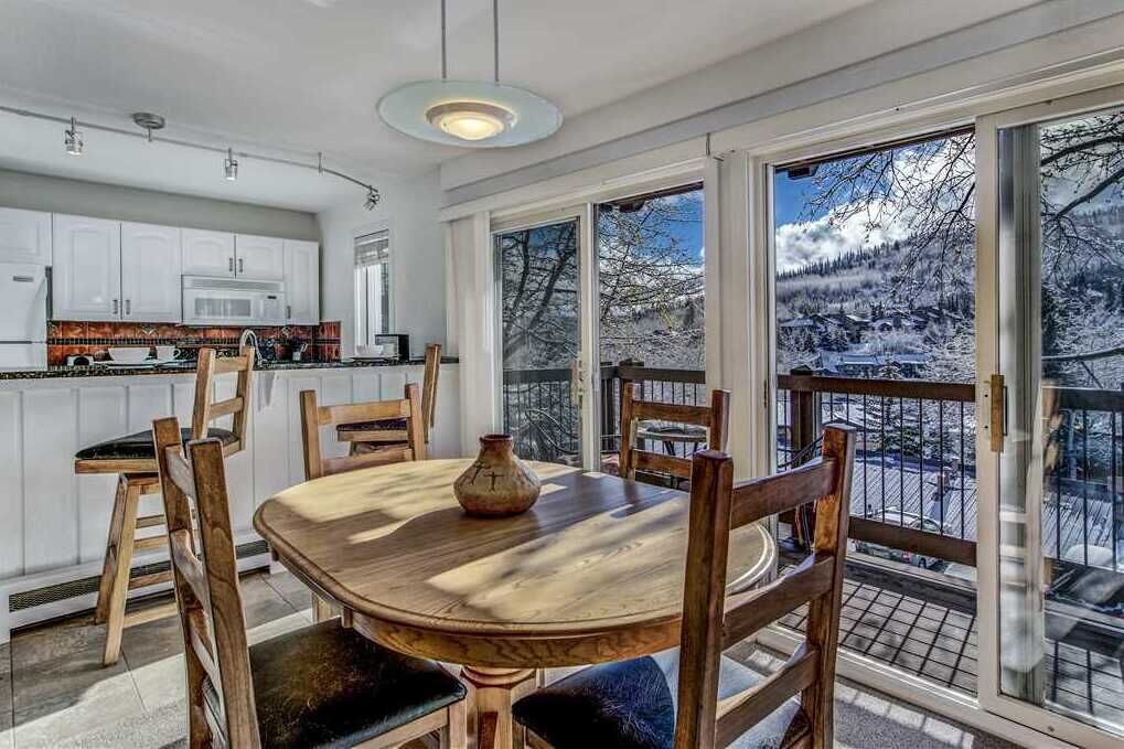 A dining area with a wooden table and chairs, a vase, and a view of a snowy mountain landscape through large windows.