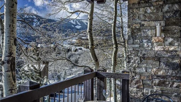 A balcony with a stone wall, a metal railing, and a view of snow-covered mountains. - Woodbridge Condos by Snowmass Vacations (Snowmass Village)