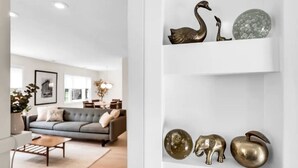 A modern living room with a grey sofa, a wooden coffee table, and a white wall with decorative metal sculptures. - Benelo | Midcentury Modern Single-Level Home, 3 BR (Sioux Falls)