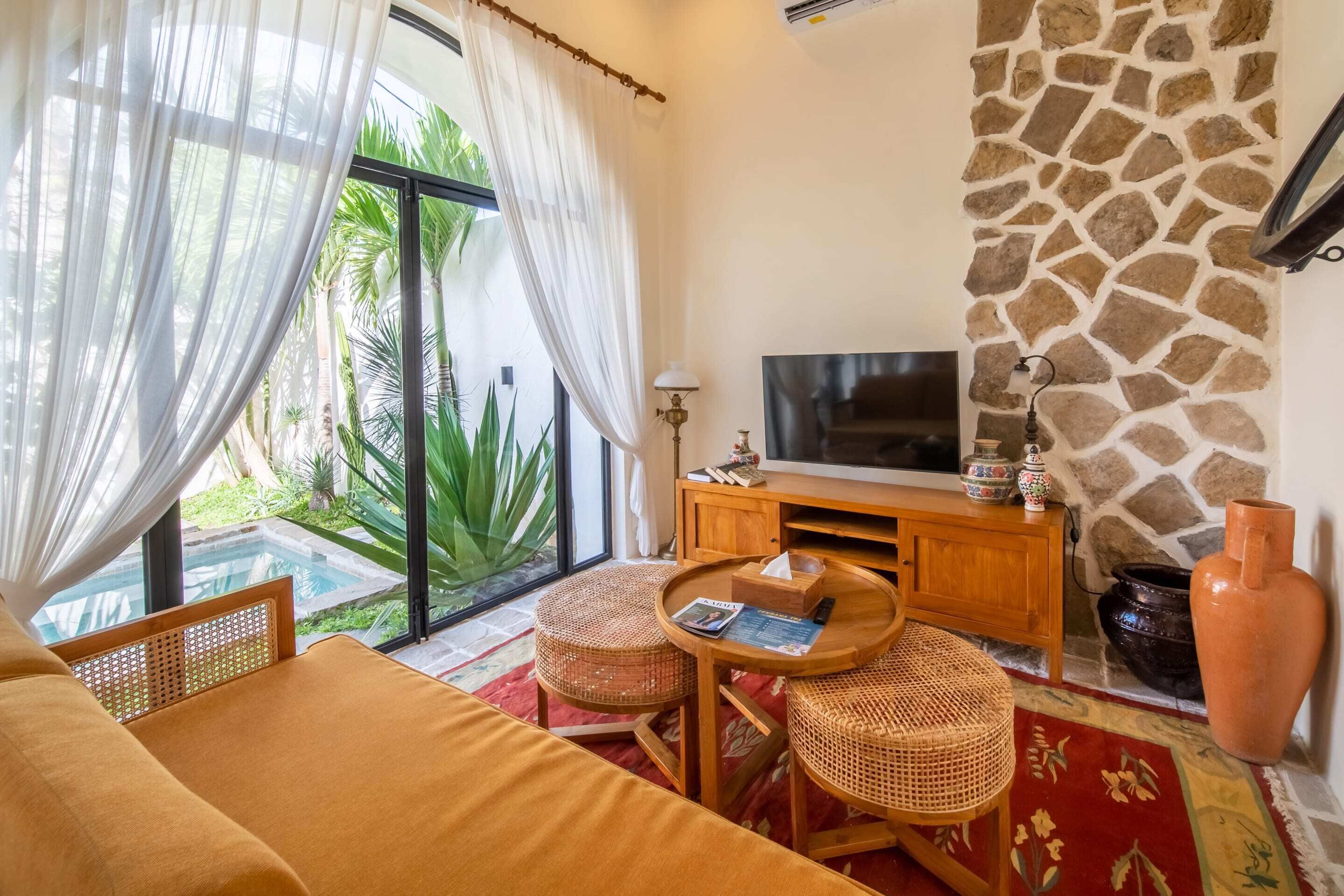 Una habitación con cama, televisor, muebles de mimbre, pared de piedra y vista a zonas verdes.