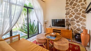 Una habitación con cama, televisor, muebles de mimbre, pared de piedra y vista a zonas verdes.