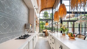 A modern kitchen with a geometric backsplash, a long countertop, and a view of the outdoors through large windows. - Villa Yukiko, 4BR Modern Tropical Design Villa (Canggu)