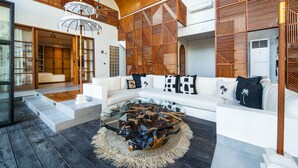 A spacious living area with a white sofa, a glass coffee table, and a wooden partition with geometric patterns. - Villa Yukiko, 4BR Modern Tropical Design Villa (Canggu)
