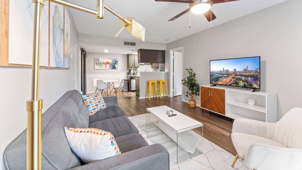 A modern living room with a gray sofa, a white coffee table, and a ceiling fan. - SoCo 2BR corner suite, king bed, fast WiFi w/ pool (Austin)