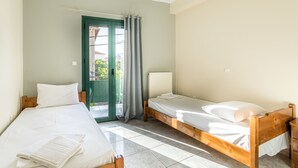 Ein Zimmer mit zwei Einzelbetten, einem hölzernen Kopfteil, einer grünen Tür und Blick ins Freie.