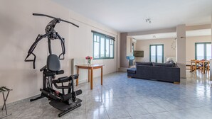 Ein geräumiger Wohnbereich mit einem feststehenden Ergometer, einer Couch, einem Esstisch und Blick durch große Fenster nach draußen.