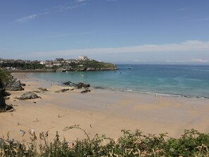 A coastal beach with a rocky shoreline, a sandy beach, and a hill with buildings in the background. - 5 Quay Court (Newquay)
