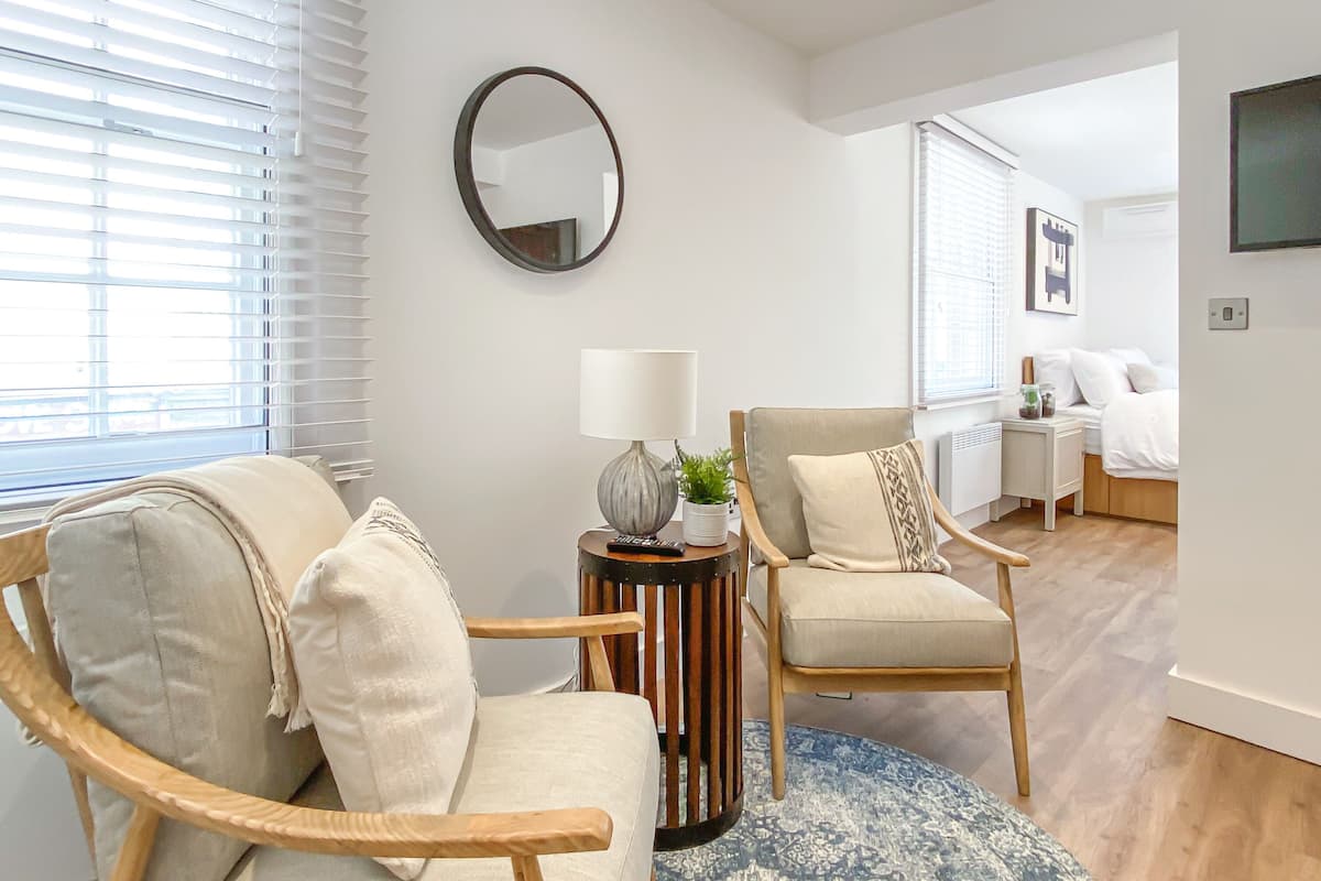 Een moderne woonkamer met twee houten stoelen, een ronde salontafel en een kamerbreed tapijt met een patroon.