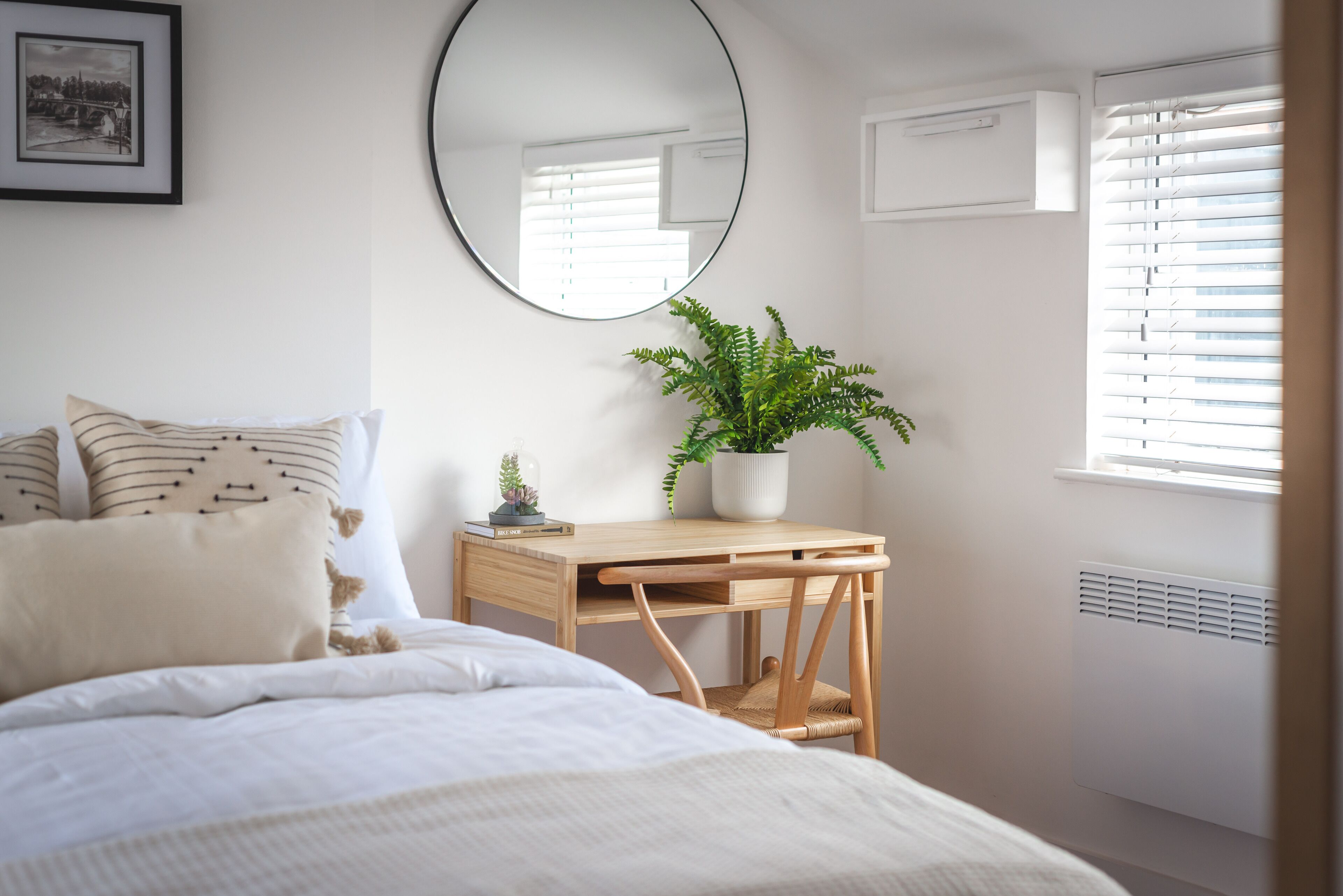 Une chambre à coucher avec un lit, un bureau en bois, une plante en pot, un miroir et un radiateur.
