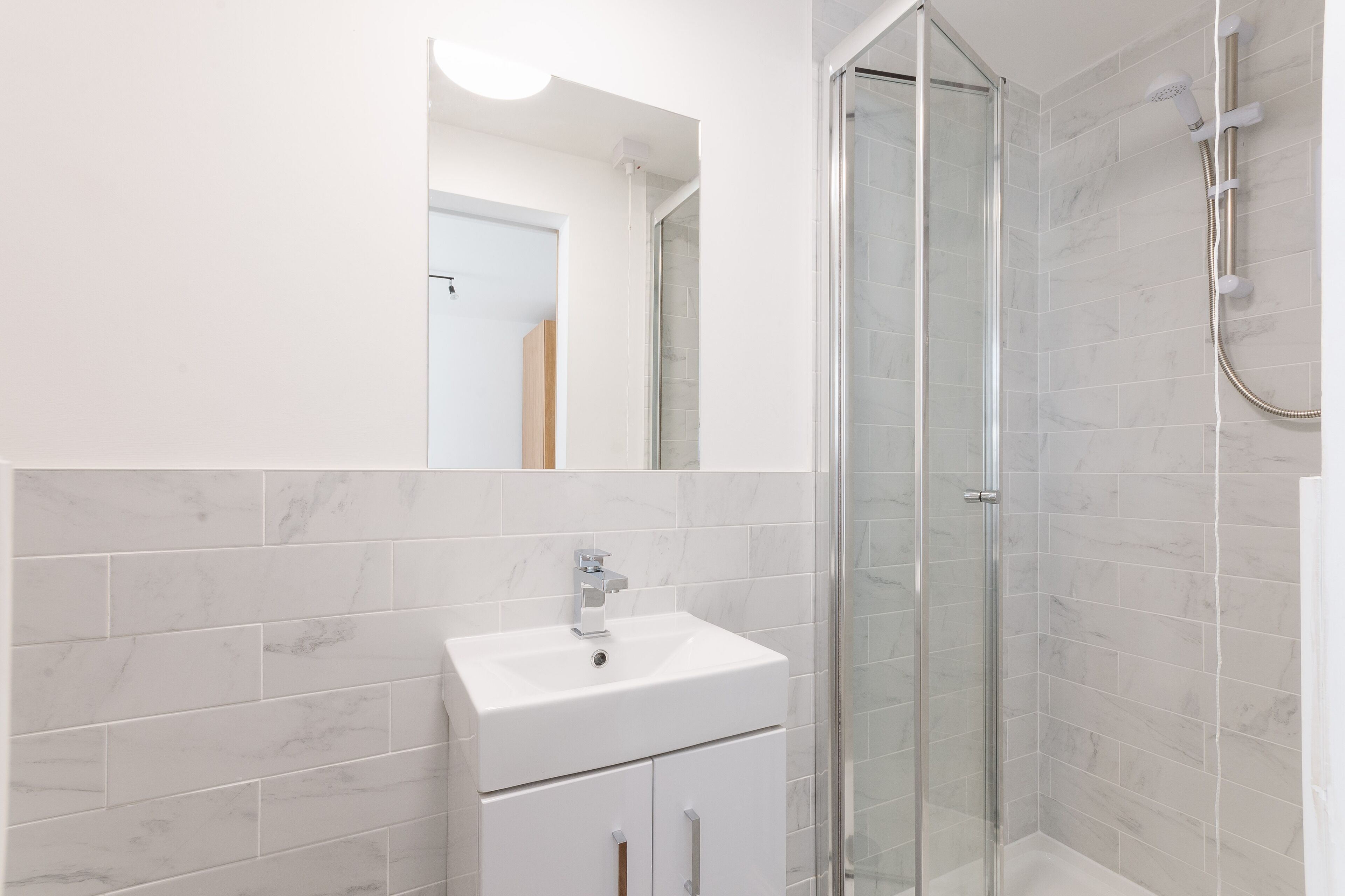 A modern bathroom with a glass shower enclosure, a white sink, and a large mirror.