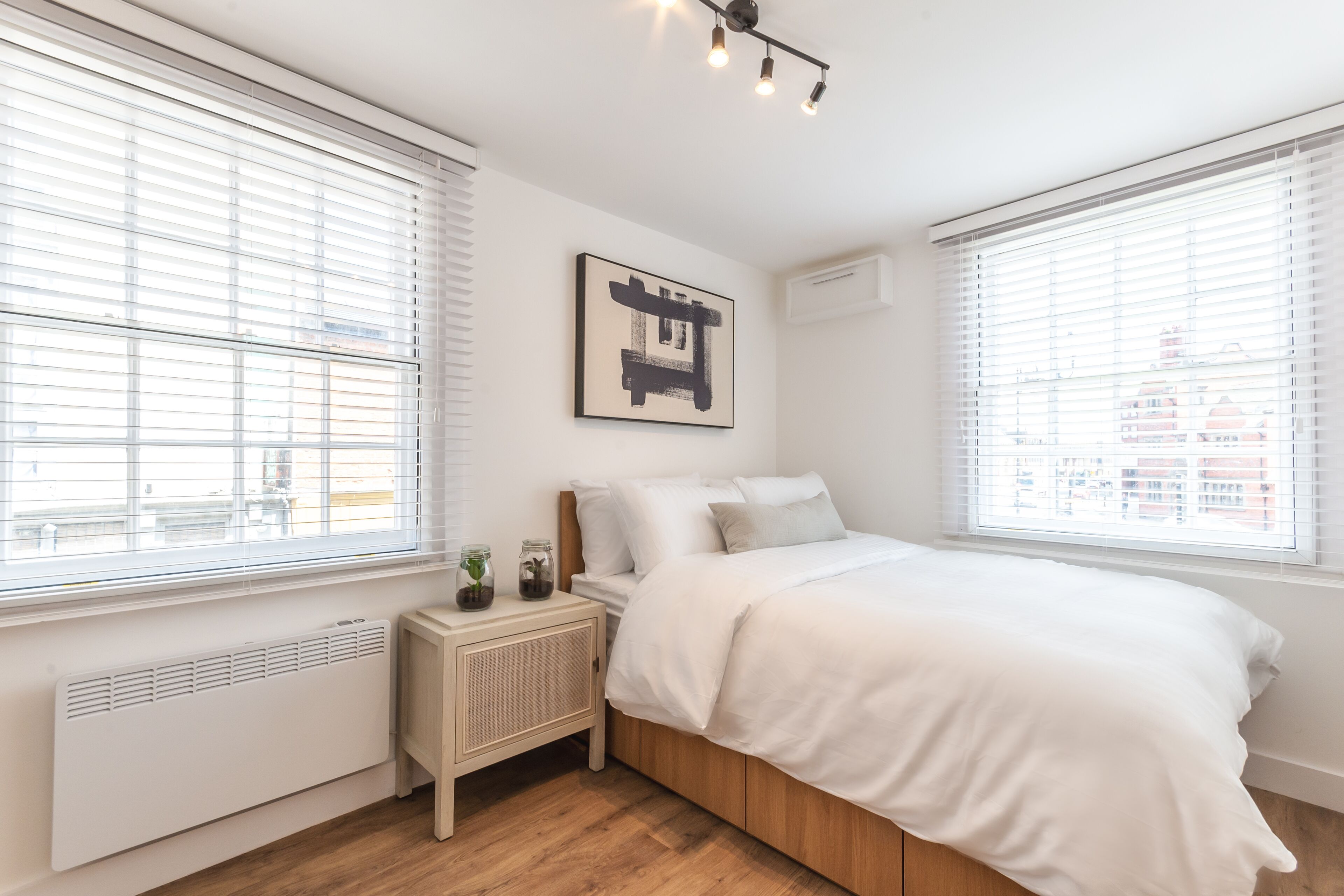 A bedroom with a bed, bedside tables, a radiator, and a window with blinds.
