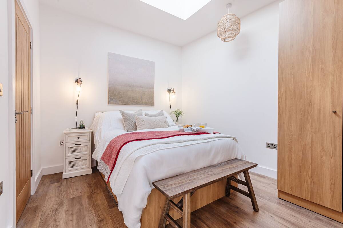 Een slaapkamer met een bed, nachtkastjes, een bankje, een kledingkast en een dakraam.