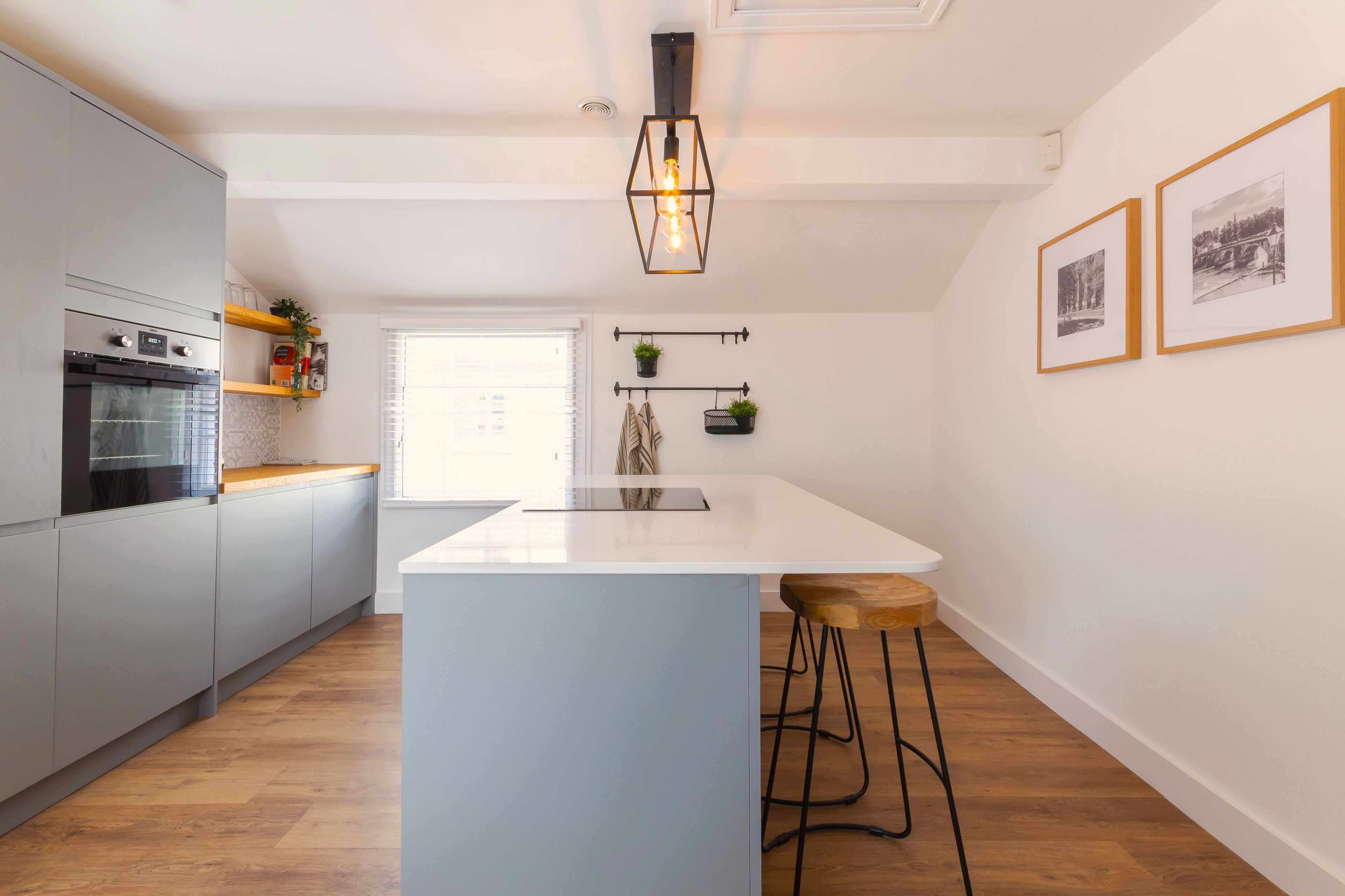 Une cuisine moderne avec des meubles gris, un îlot central blanc, des tabourets en bois et un luminaire suspendu.