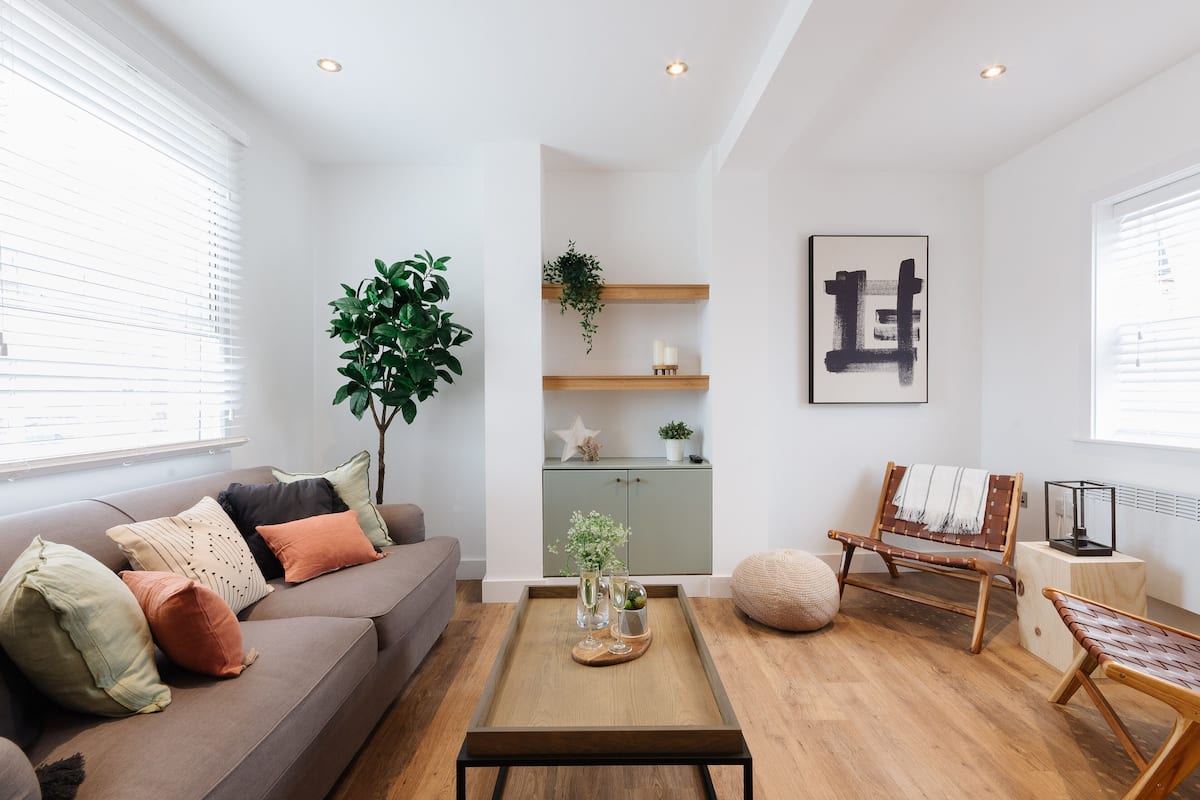 Een moderne woonkamer met een bank, salontafel en een zitbank. Er staat een plant, een kast en een lijst met kunst aan de muur.