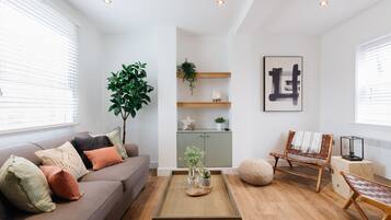 A modern living room with a sofa, coffee table, and a bench. There is a plant, a cabinet, and a framed artwork on the wall.