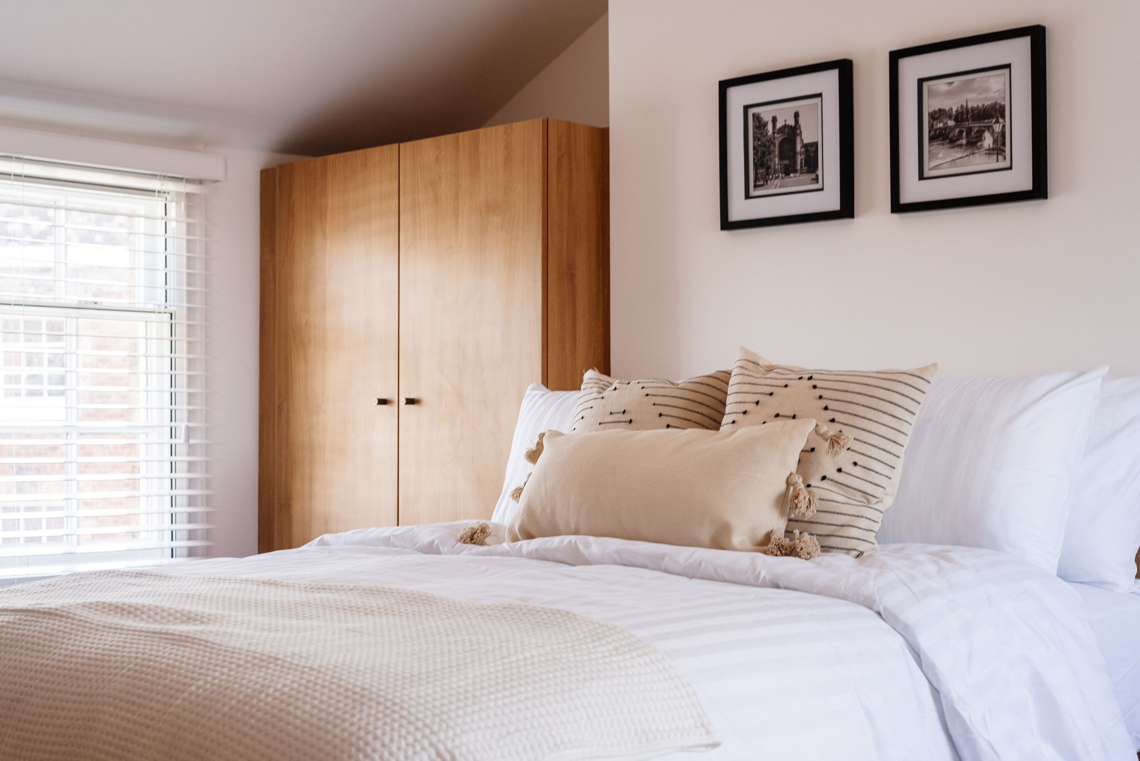 A bedroom with a bed, white bedding, a wooden wardrobe, and two framed pictures on the wall.