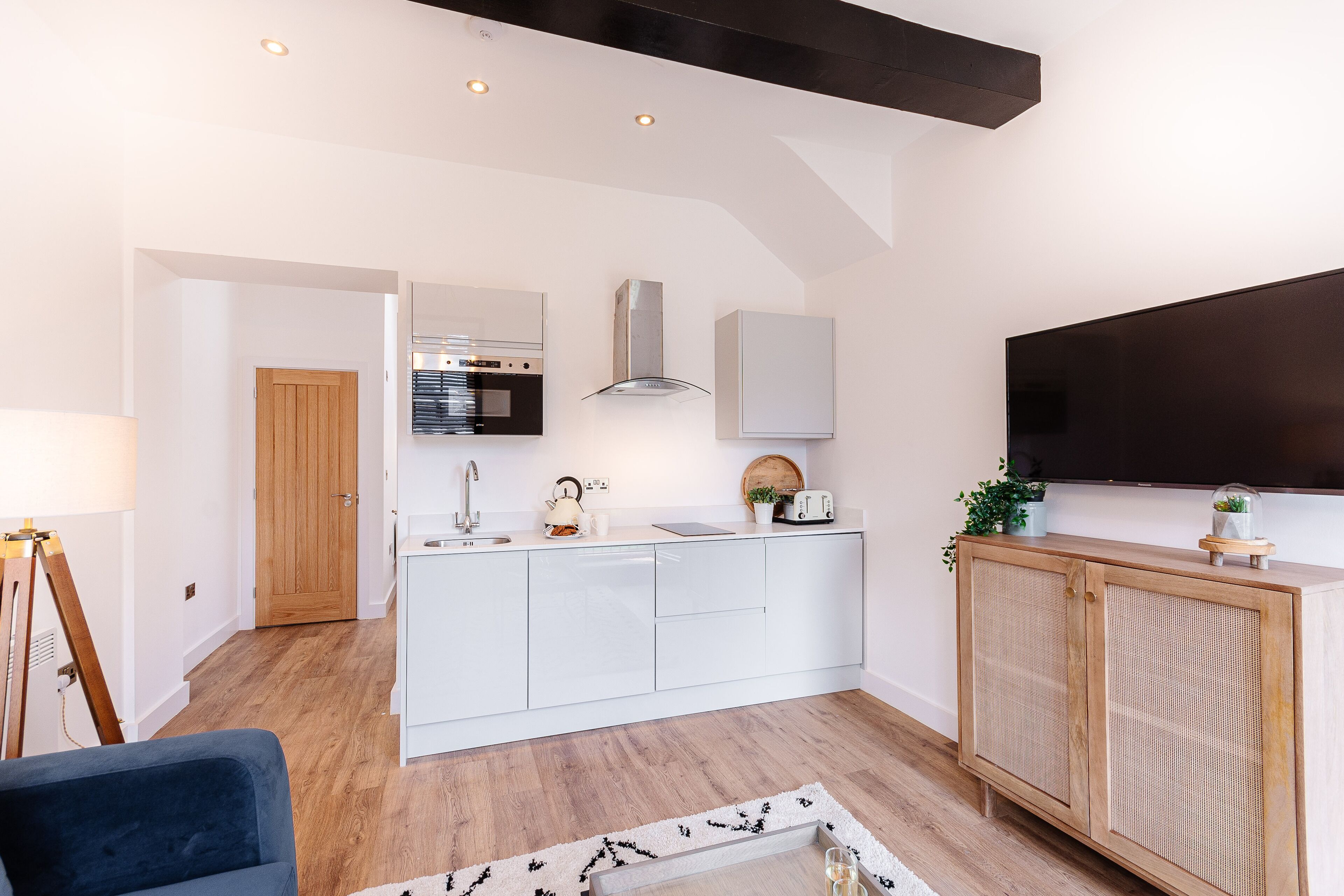 A modern kitchen with white cabinets, a built-in oven, and a large TV above the counter.