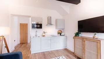 A modern kitchen with white cabinets, a built-in oven, and a large TV above the counter.