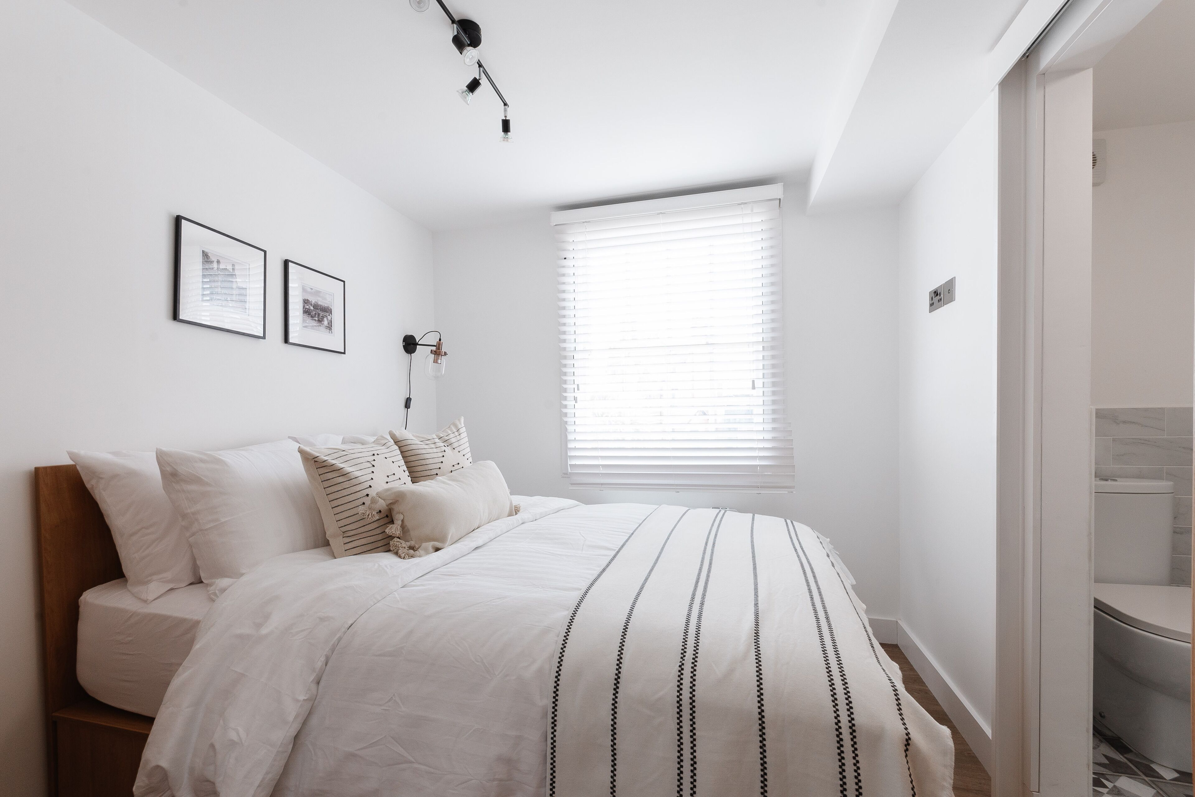 Una camera da letto con un letto, una finestra con persiane e un punto luce fissato al muro.