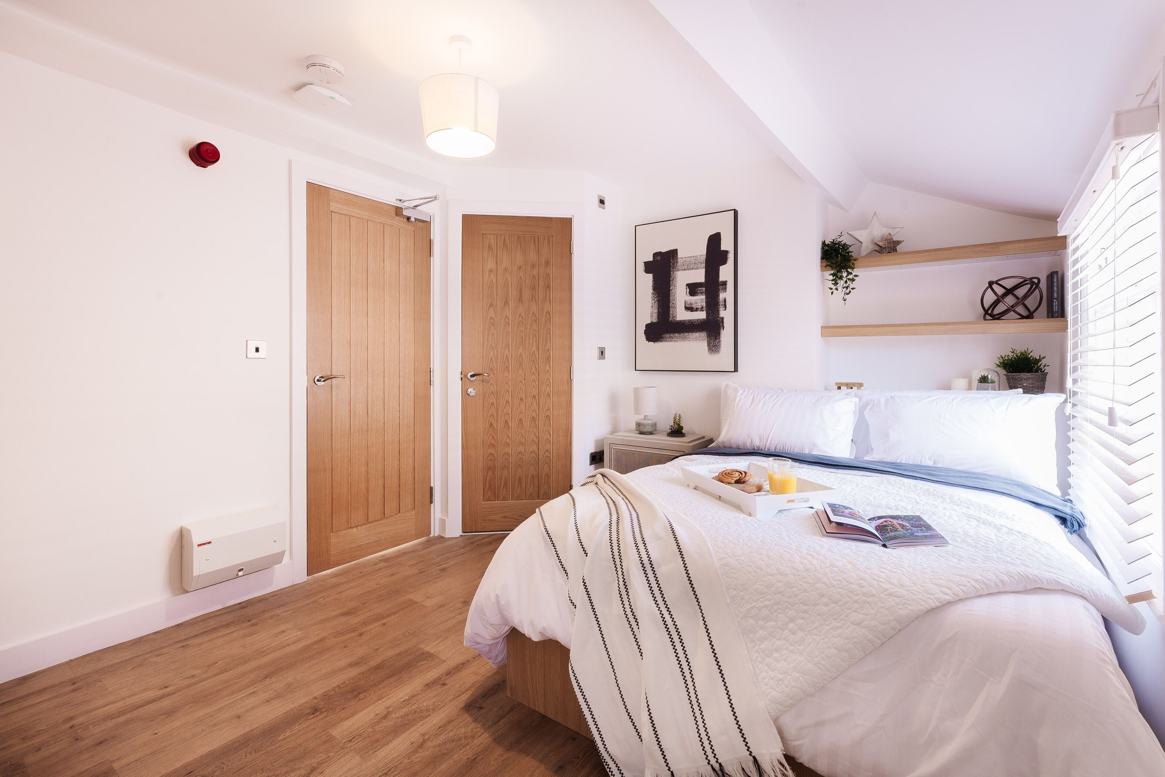 Un dormitorio con cama, mesita de noche, repisa en la pared y una puerta.