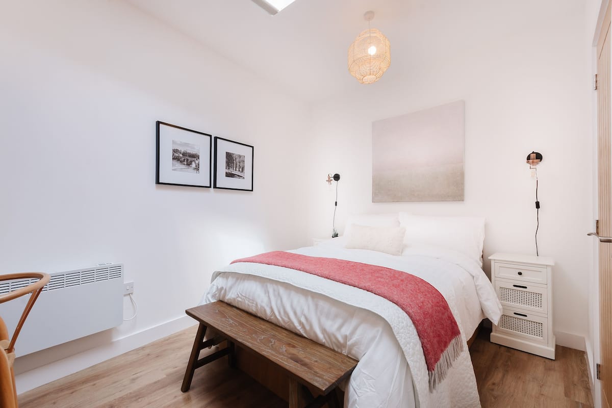 Een slaapkamer met een bed, nachtkastjes, een bankje, een radiator en kunst aan de muur.