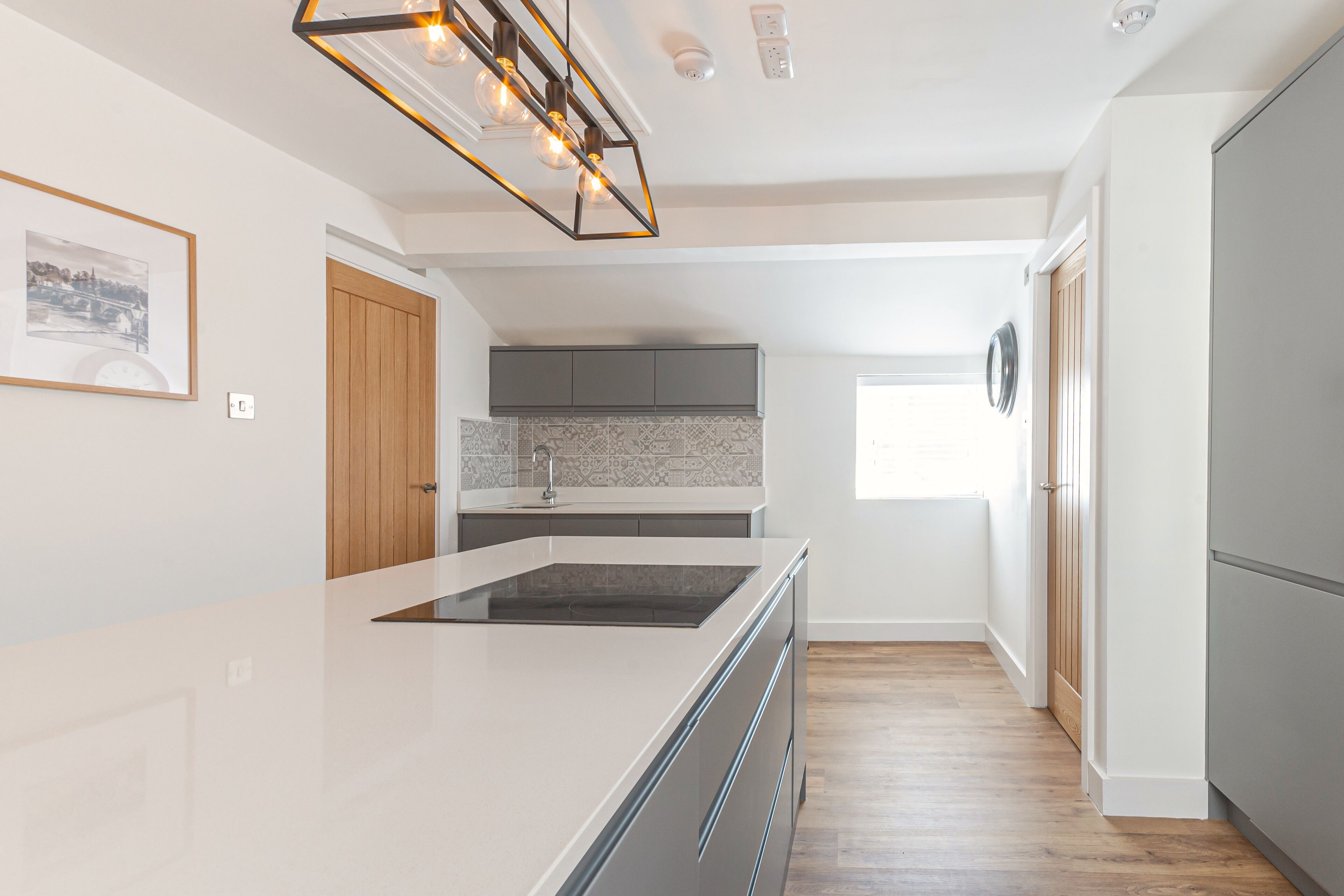 A modern kitchen with a central island, grey cabinets, and a wooden door.