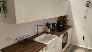 Eine Küche mit weißen Schränken, einer Holzausziehtafel, einem Spülbecken, einem Wasserkocher und einer Uhr an der Wand.