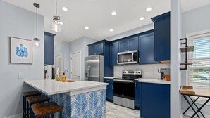 A modern kitchen with blue cabinets, stainless steel appliances, and a white island with bar stools. - Newly- updated home, a block away from the beach! (Miramar Beach)