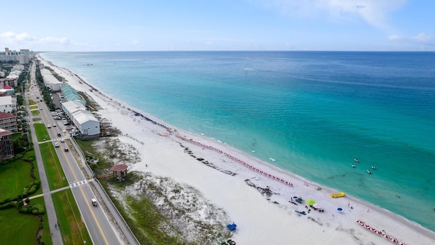 A coastal road with a beach on the right, lined with buildings and a clear sky. - Newly- updated home, a block away from the beach! (Miramar Beach)