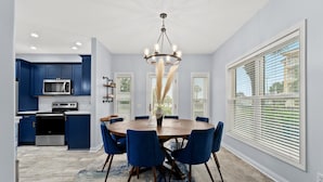 A modern kitchen with blue cabinets, a round dining table with blue chairs, and a chandelier. - Newly- updated home, a block away from the beach! (Miramar Beach)