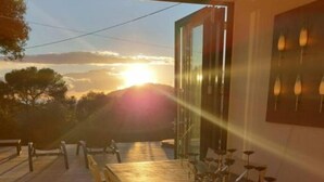 Un espace de restauration en plein air avec une longue table et des chaises, une batterie et une vue sur le coucher du soleil.
