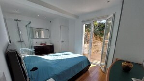 Une chambre moderne avec un grand lit, une table de chevet avec une lampe, une commode et une porte-fenêtre coulissante donnant sur un espace extérieur.