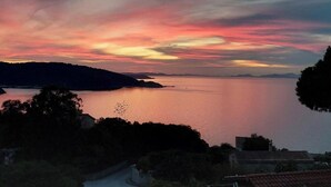 Un paysage côtier avec une mer calme, une route menant à un bâtiment et une côte lointaine.