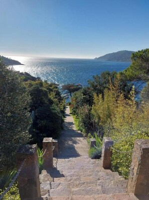 A stone staircase leading to a coastal area with a view of the sea and hills.