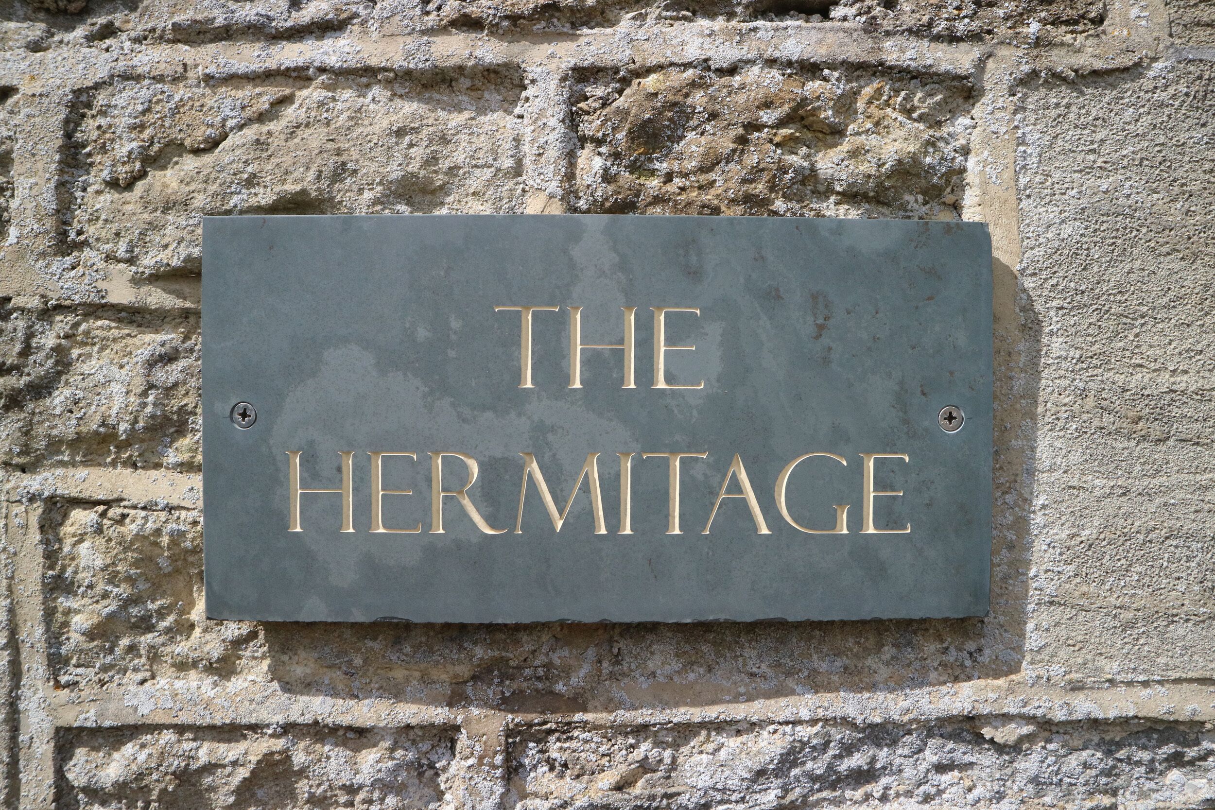 A sign with the text "THE HERMITAGE" mounted on a stone wall.